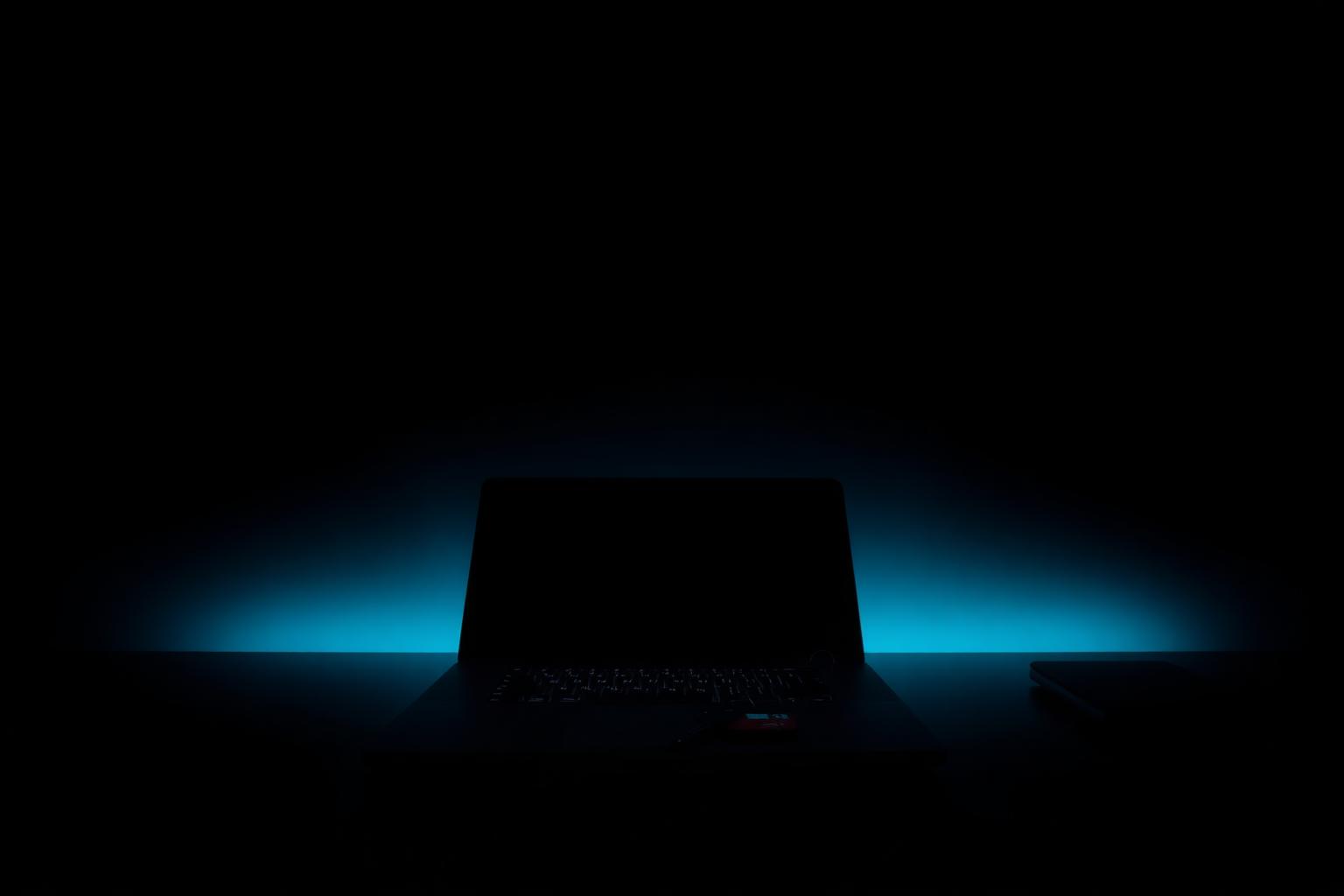 Closed laptop on a dark desk with soft blue backlight, symbolising an employee leaving and IT offboarding